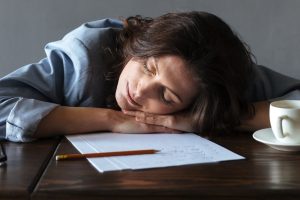 Photo of sleeping woman writer lies indoors on table near cup of coffee and and notes.